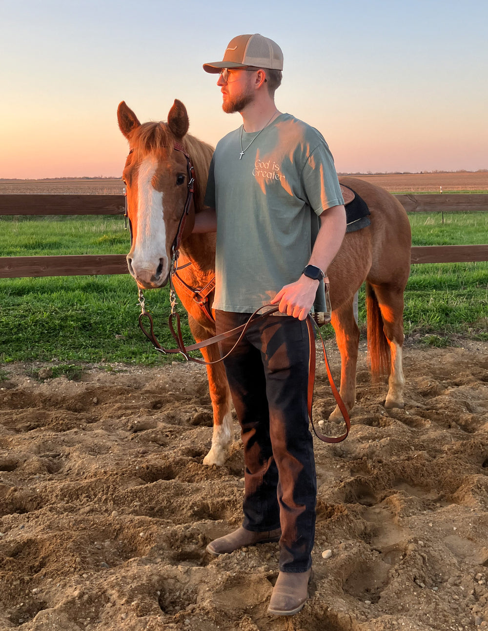 Man standing with a horse in a field at sunset
