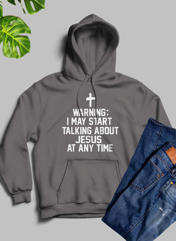 Gray hoodie with text 'Warning: I may start talking about Jesus at any time' on a gray background with jeans and a plant.