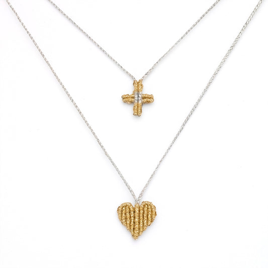 Gold heart and cross pendant on a silver chain against a white background