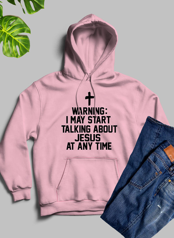 Pink hoodie with text 'Warning: I may start talking about Jesus at any time' on a gray background with jeans and a plant.