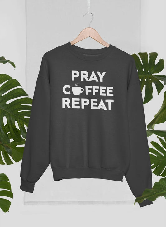 Black sweatshirt with 'PRAY COFFEE REPEAT' text on a hanger against a white background with green leaves.