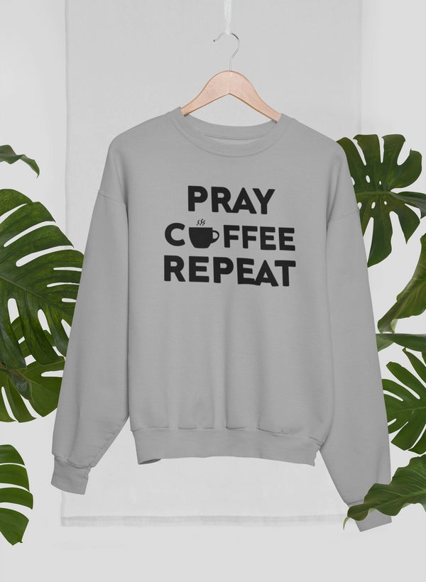 Gray sweatshirt with 'Pray, Coffee, Repeat' text on a hanger with green leaves in the background