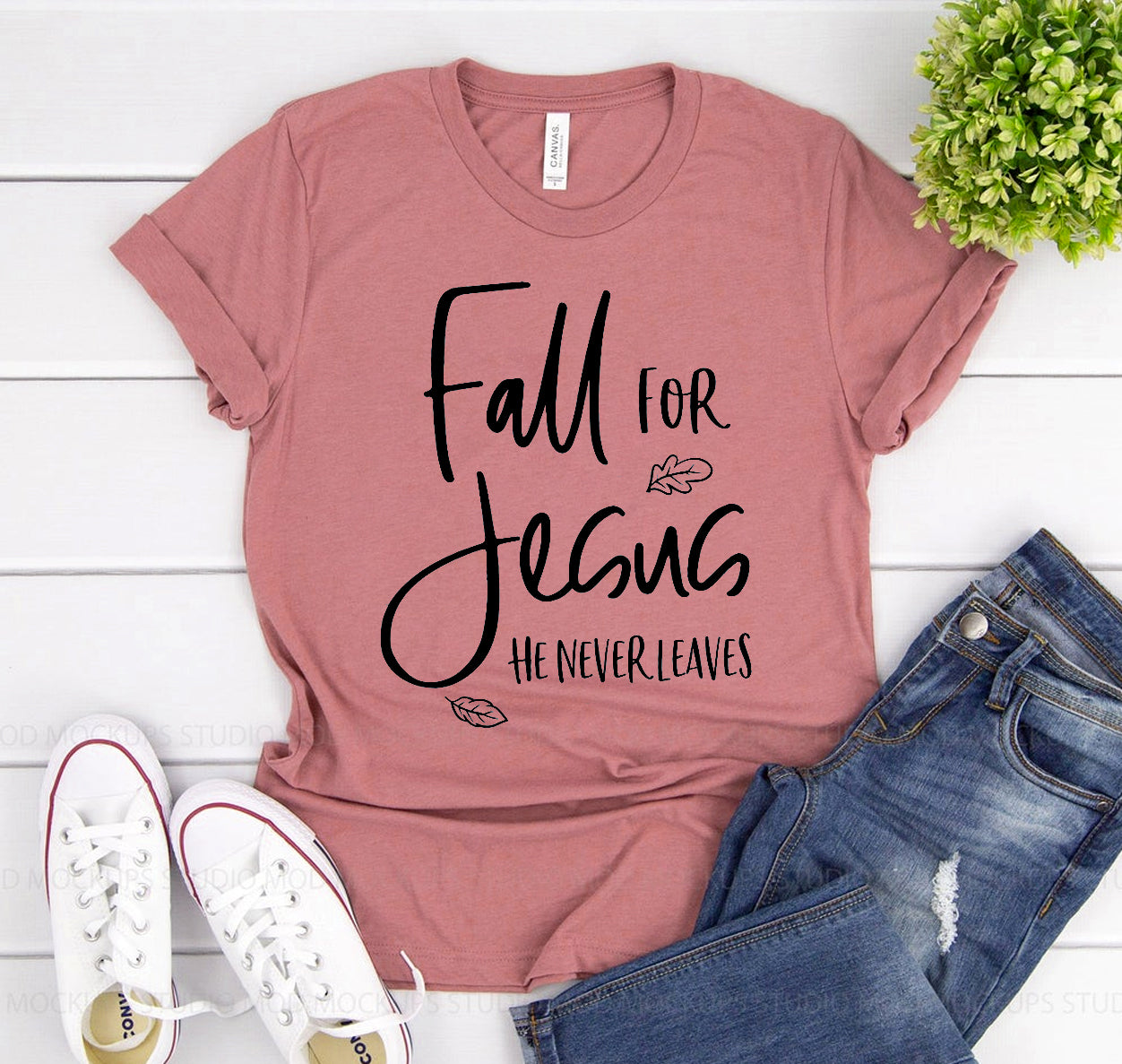 Pink t-shirt with 'Fall for Jesus He Never Leaves' text, paired with jeans and sneakers on a white background.