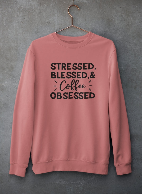 Pink sweatshirt with text 'Stressed, Blessed & Coffee Obsessed' on a gray background