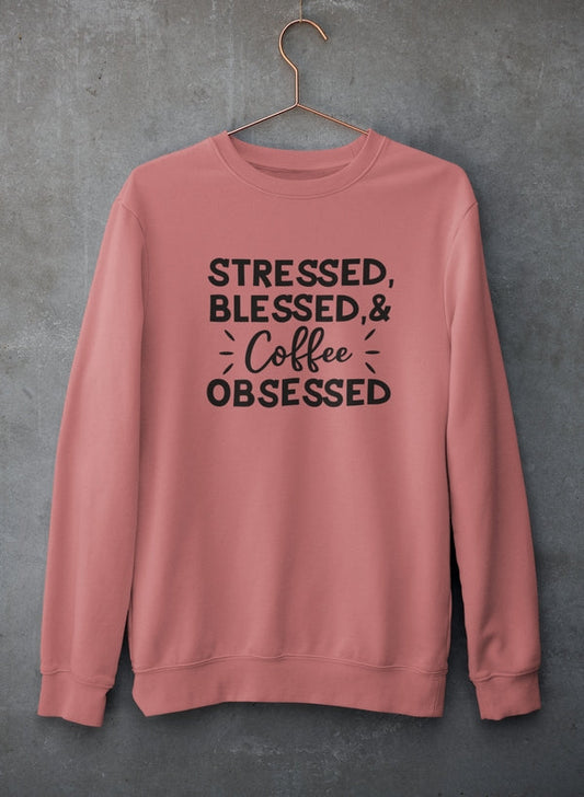 Pink sweatshirt with text 'Stressed, Blessed & Coffee Obsessed' on a gray background